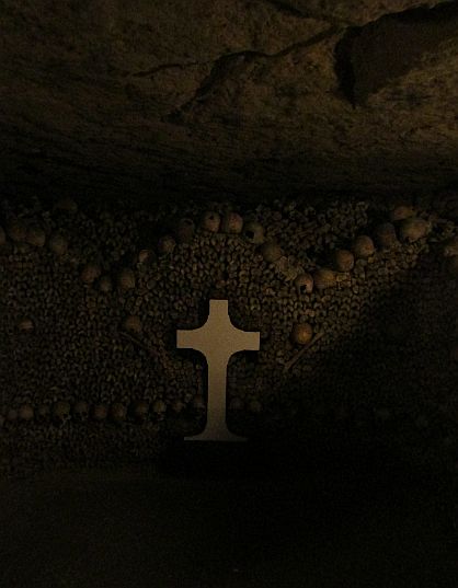 A cross and three mounds of bones in the Paris Catacombs. 