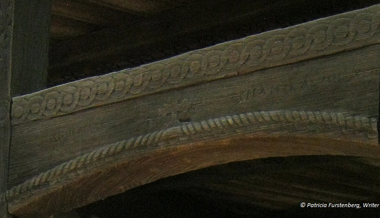 Symbols carved in wood in the upper beam of a porch: cope detail, cross, infinity column.