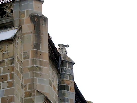 the statue of a child peering down atop the roof near the Golden Portal, Black Church, Brasov