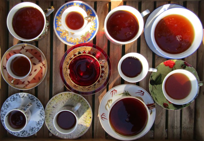 a tray of various size teacups filled with reddish-brown tea on a wooden tray in the golden hour