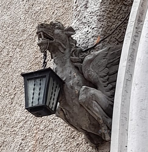 carved stone griffon or grotesque holding a black metal lantern hanging from its mouth